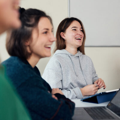 Zwei Frauen sitzen an einem Tisch mit Laptop und Tablet.